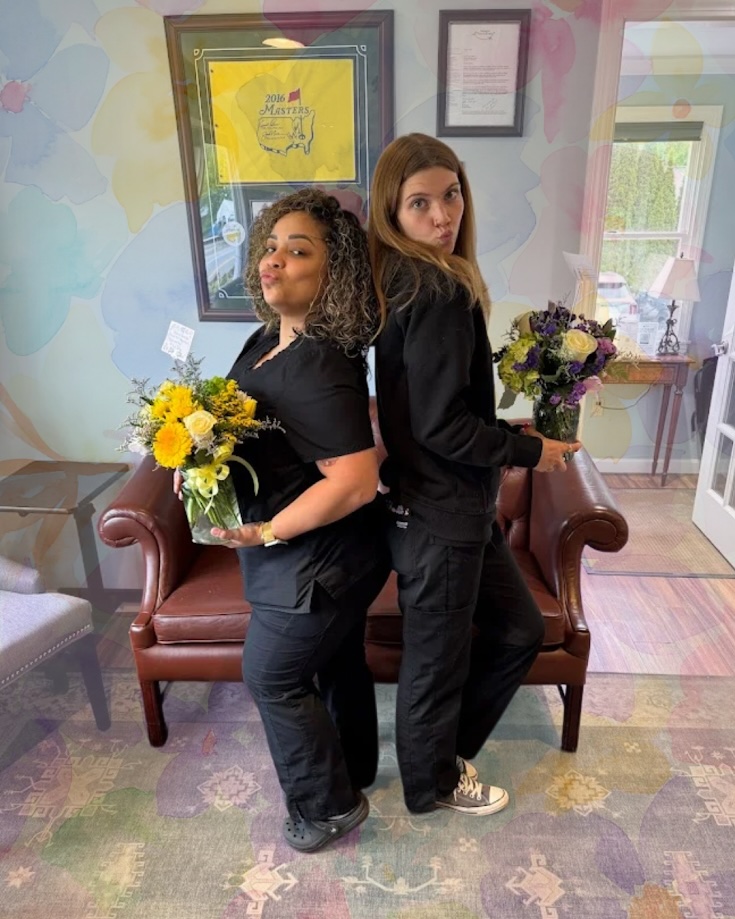 Dental team members holding bouquets in front of a floral backdrop in the waiting room in Lunenburg