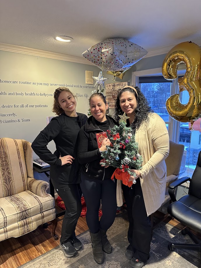 Three dental team members holding a mini Christmas tree during an office holiday celebration in Lunenburg