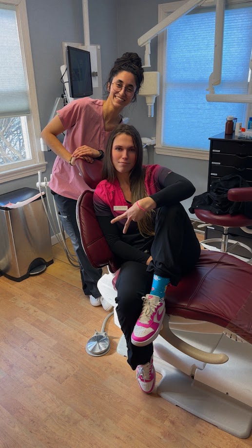 Two dental team members posing playfully in a treatment room chair in Lunenburg