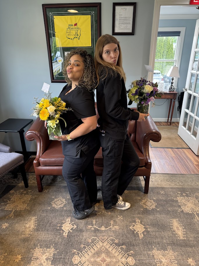 Two dental team members posing back to back with flower bouquets in the reception area in Lunenburg