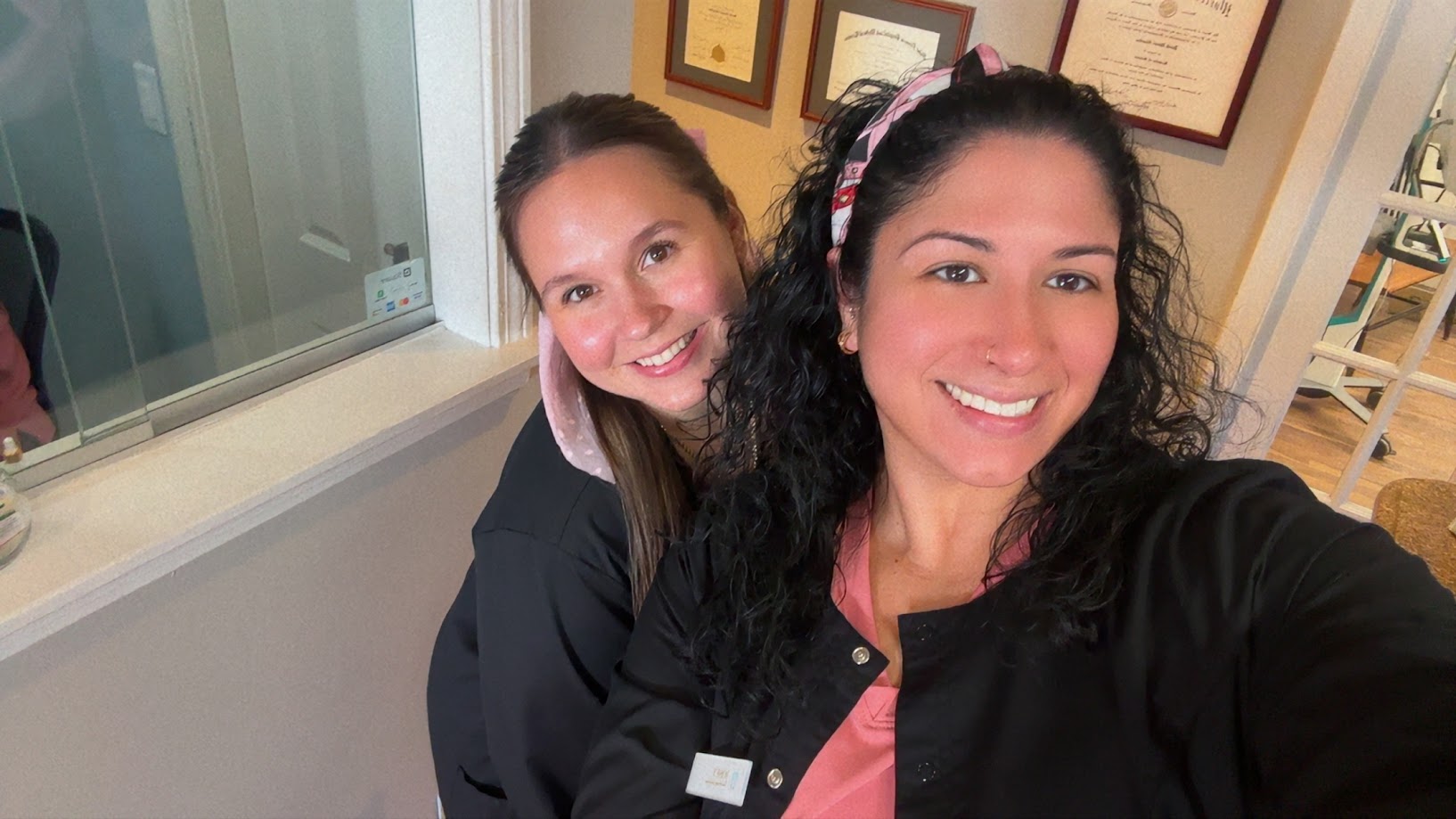 Two dental team members taking a smiling selfie by the diploma wall in Lunenburg