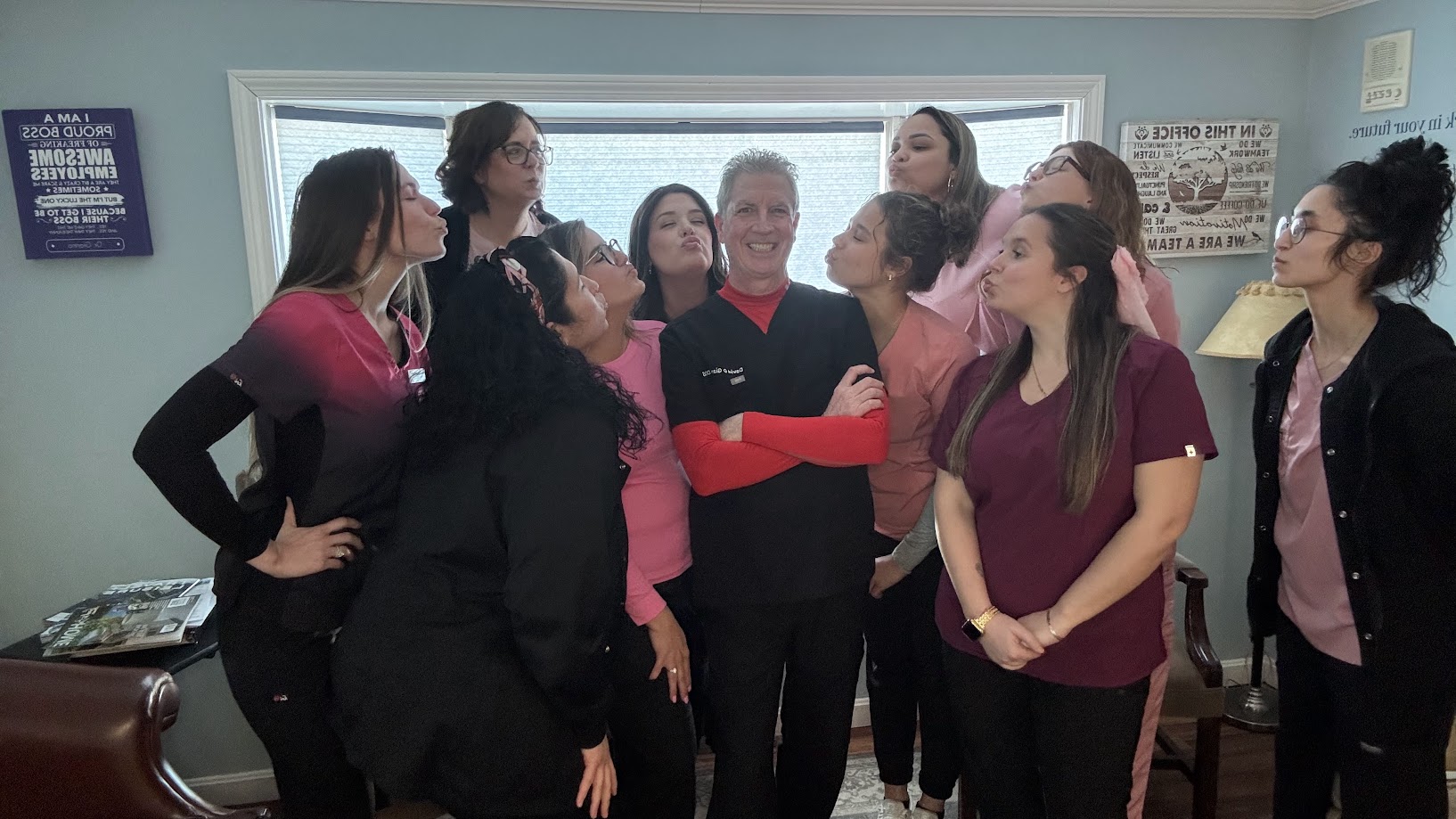 Dental team in pink and red scrubs surrounding the dentist for a playful Valentine's photo in Lunenburg